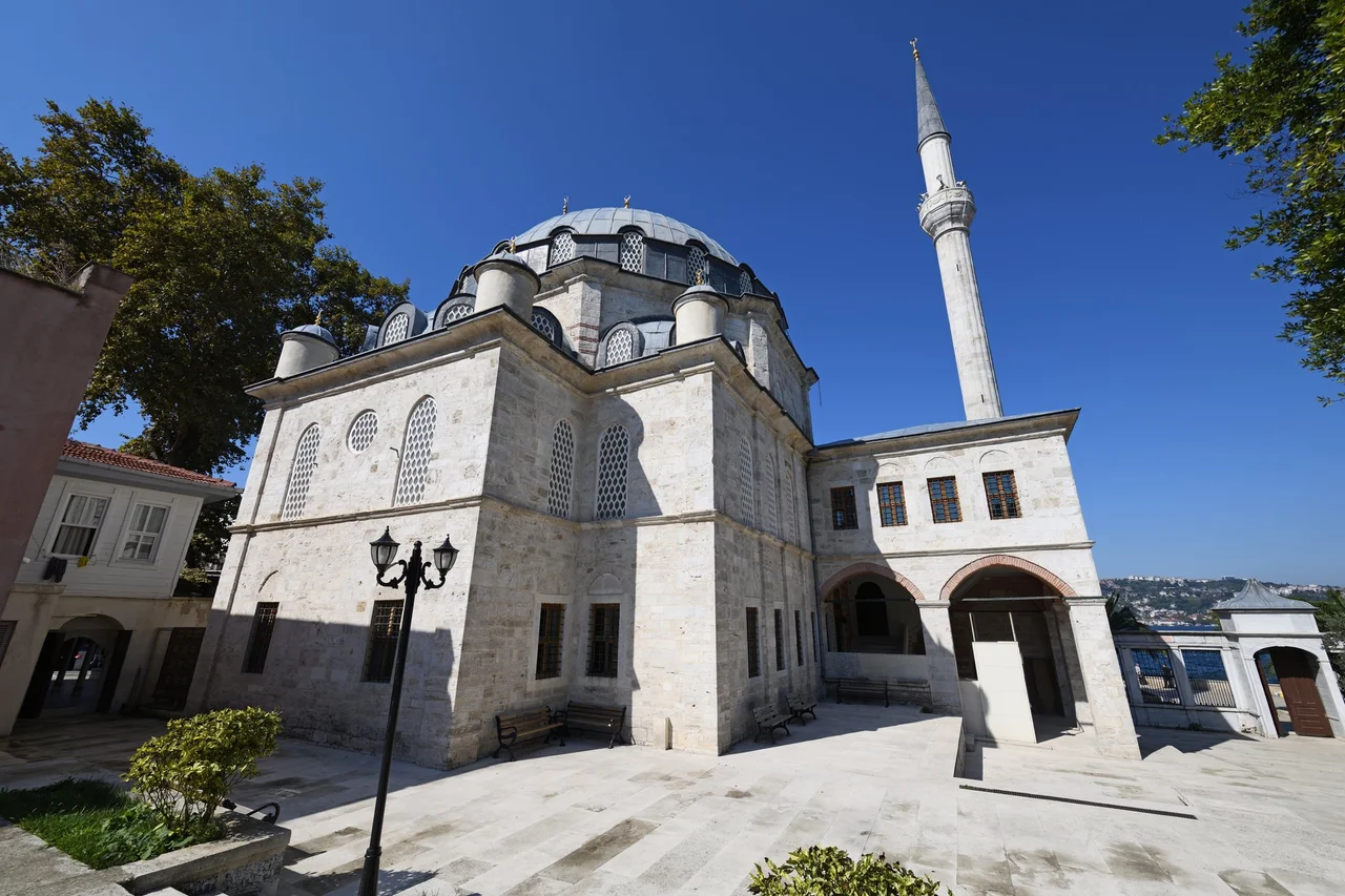 There is a courtyard on the land side of the mosque, with some utility buildings around. This is a view of the mosque from there.
The Beylerbeyi Mosque (also known as the Hamid-I Evvel Mosque) is an Ottoman Baroque mosque, built in 1777-1778, and was commisioned by Abdülhamid I in the memory of his mother Rabia Sermi Sultan. Its architect was maybe (in many cases the actual architect was not known, but a “chief architect” who oversaw all sort of building sites in town was often mentioned) Mehmed Tahir Ağa.
The dome has been replaced as the original one was damaged, and the two minarets were not in the original design but built in 1810-11. The mosque is on the side of the Bosporus in a neighbourhood called Beylerbeyi itself.
In its front there is a courtyard, and in front of that fishermen are busy with their rods, surrounded by waiting cats.