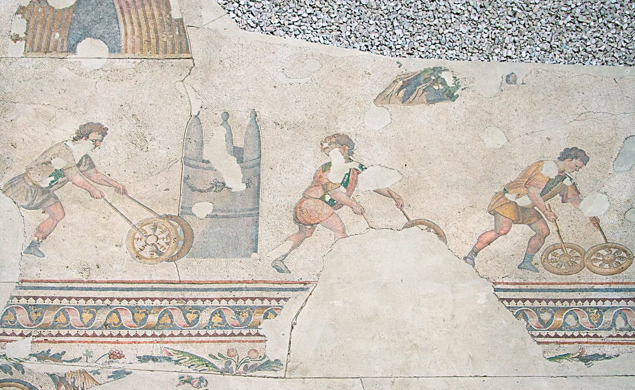 Children trundling hoops in the arena. Four children (one out of the picture) are each trundling two hoops, and turning around cones as they are used in an arena. Them wearing blue or green shawls refers to the Blues and Greens factions in the Constantinople area. Such scenes can often be found on Roman sarcophagi. The museum's catalogue explains that hoop trundling was a serious sport for grown men too, and mentions several sources where it can be seen on monuments and such.