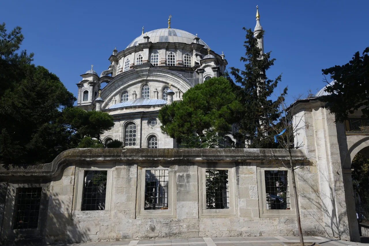 A view from outside the walled-off area the mosque is on. There are many trees surrounding the mosque, as a result it was impossible to me to take a picture showing the whole.
From the Wikipedia: ”Big Selimiye Mosque (Turkish: Büyük Selimiye Camii), often known simply as Selimiye Mosque, is situated in the district of Üsküdar in İstanbul, Turkey, right across the Selimiye Barracks. The mosque was commissioned by Ottoman Sultan Selim III (reigned 1789–1807) and completed in 1801, however its main architect is unknown.
The Big Selimiye Mosque has a western style, a wide courtyard and four entrance doors. After the completion of the mosque, the original minarets were thought to be too thick, and later shaved. The mosque is seen as a masterpiece of carpentry and marble work. The dome is 14.6 m (48 ft) wide, has five windows and supported by four half domes. The Big Selimiye Mosque has a "muvakkithane" for keeping prayer times and a water fountain. “ 

As for the Western Style, this can be read as "Ottoman Baroque".