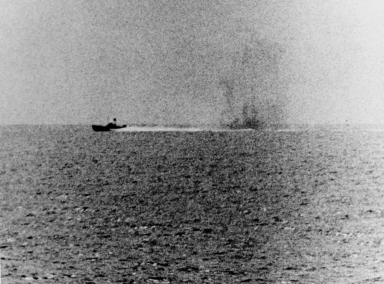 Photograph taken from the U.S. Navy destroyer USS Maddox (DD-731) during her engagement with three North Vietnamese motor torpedo boats in the Gulf of Tonkin, 2 August 1964. The view shows one of the boats racing by, with what appears to be smoke from Maddox' shells in its wake.