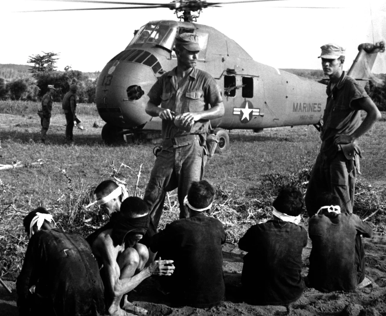 Viet Cong prisoners wait in front of a U.S. Marine Corps Sikorsky UH-34D Seahorse helicopter of Marine medium transport squadron HMM-161, during "Operation Starlight" south of Chu Lai, South Vietnam, on 1 August 1965.