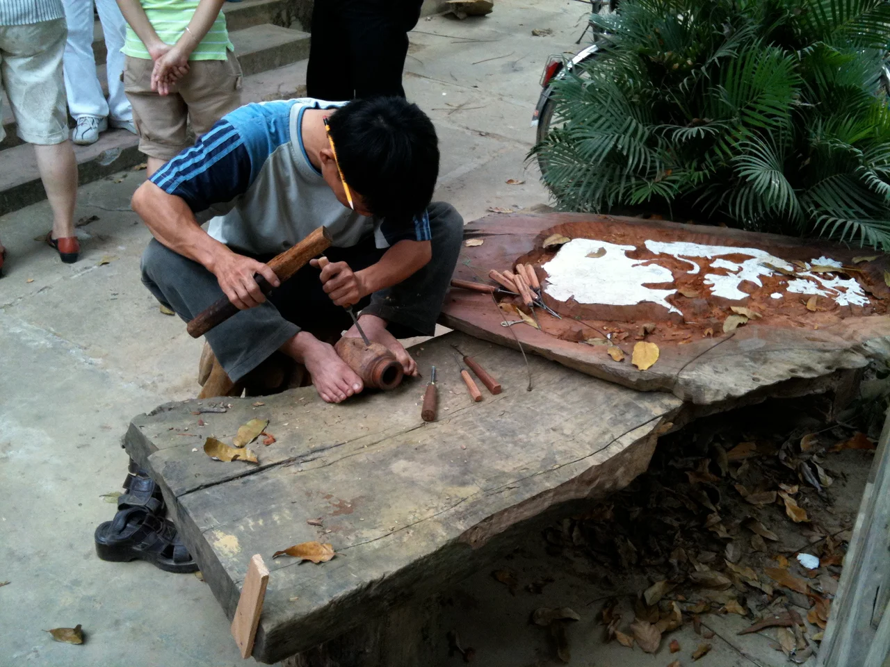 A woodworker (possibly Huynh Suong, son of master carver Huynh Ri) carves designs into a wooden pot, which he holds between his feet. Kim Bong village, Hoi An, Vietnam.