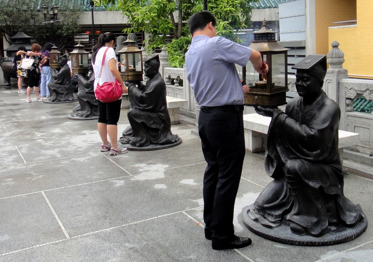 Lighting incense sticks and lamp holding statues in Wong Tai Sin Temple, Kowloon, Hong Kong