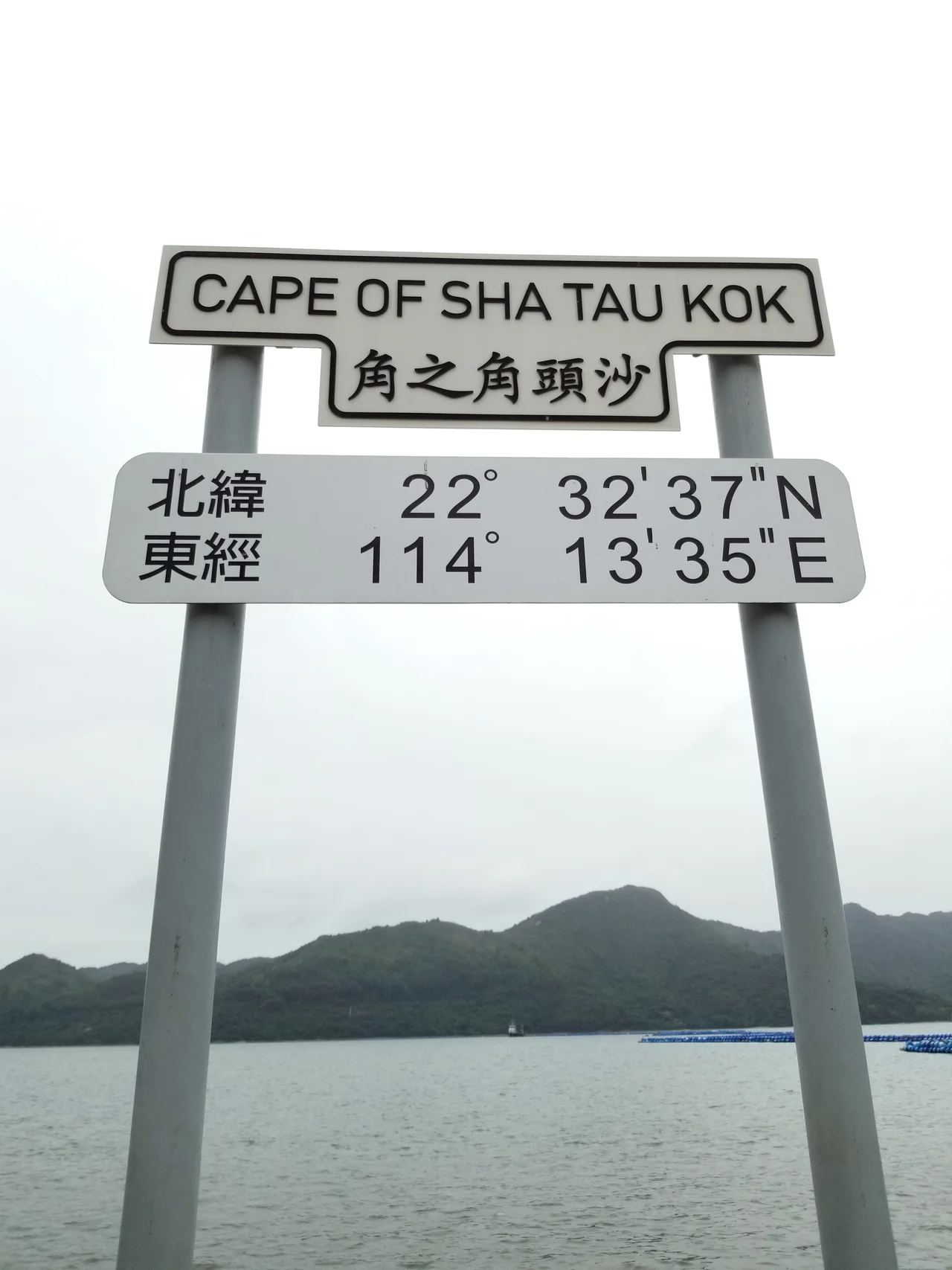 A close-up of the sign located at the Cape of Sha Tau Kok (沙頭角之角). The cape's coordinates are displayed on the sign: 22°32'37"N 114°13'35"E.